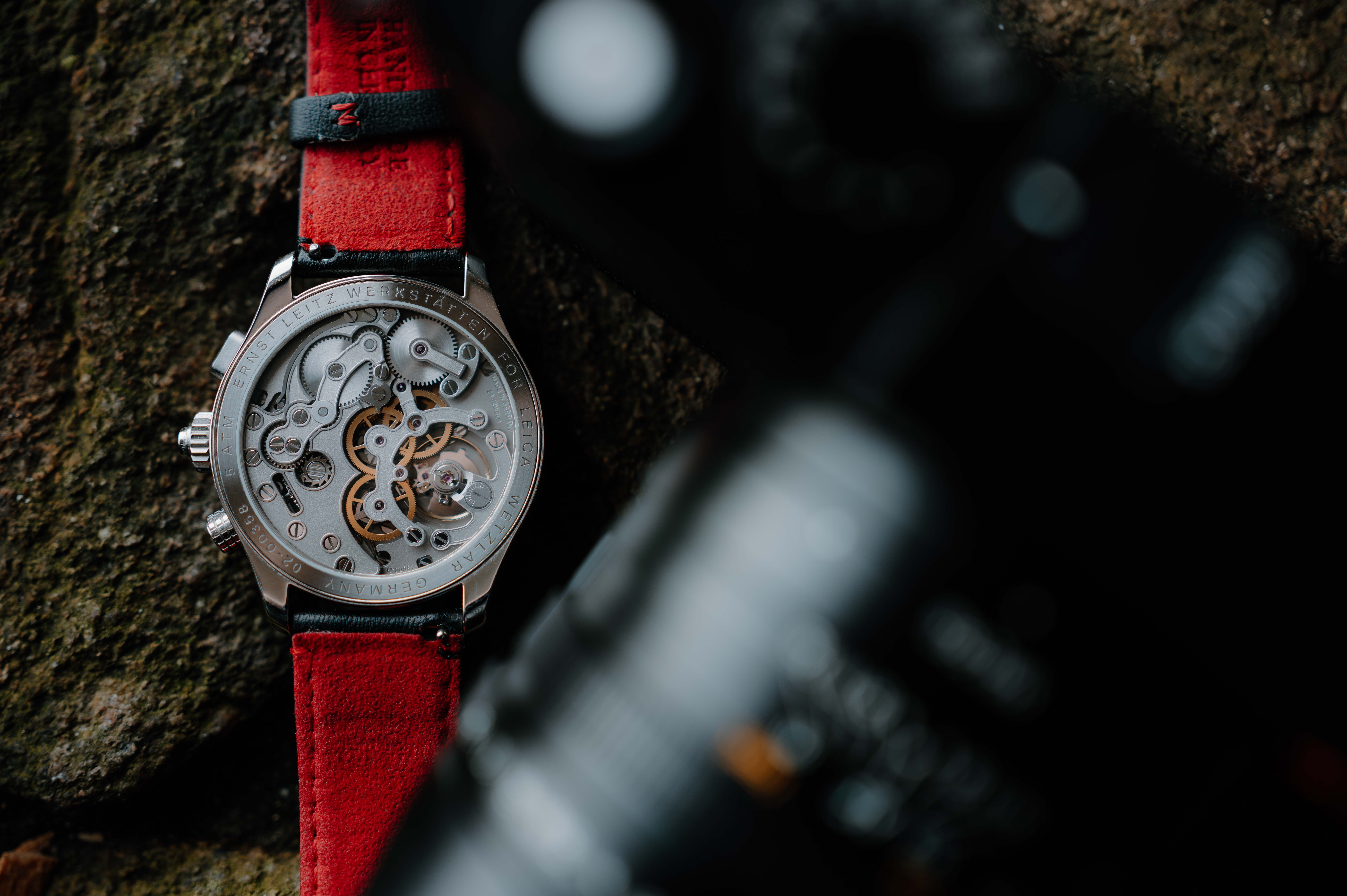 A watch with a red handle. The watch face shows the clockwork mechanism inside
